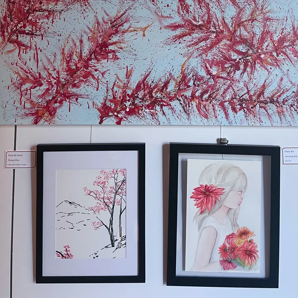 Gallery wall in the Red Pistache exhibition: Flying White framed at lower left beside a framed watercolor of a girl with red flowers, under a large painting of red branches on pale blue