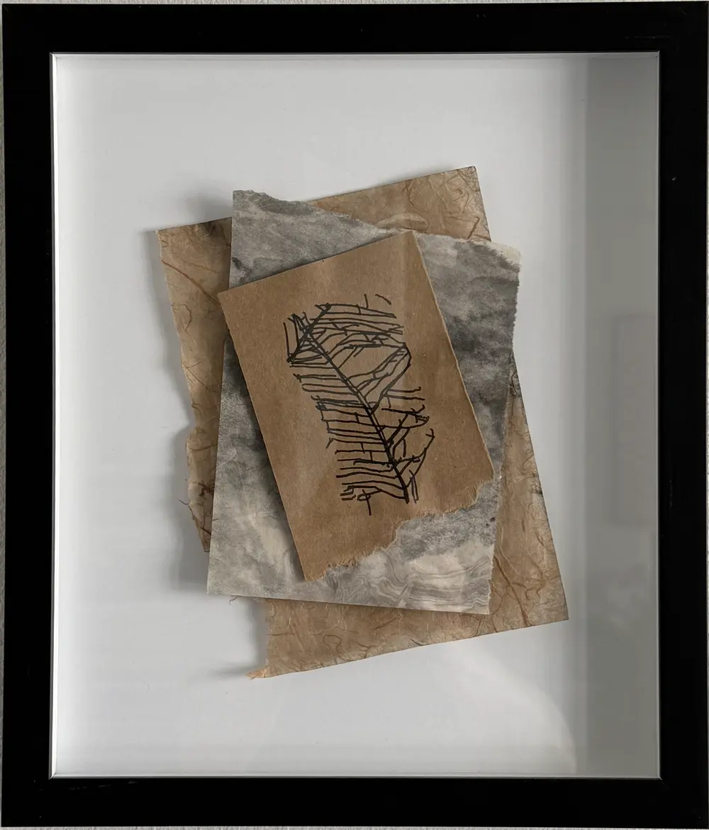 Companion collage in a matching black frame: a kraft card with a drawing like a feather or leaf spine with angular ribs, over smoky grey marbled paper and torn tan fibrous paper