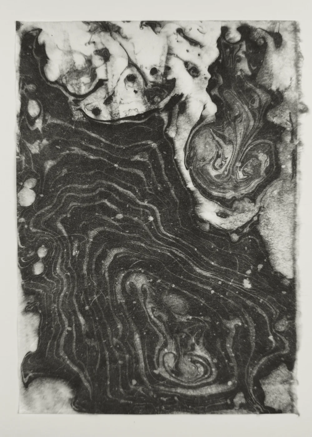 Black and white suminagashi monotype with flowing ink patterns on washi paper
