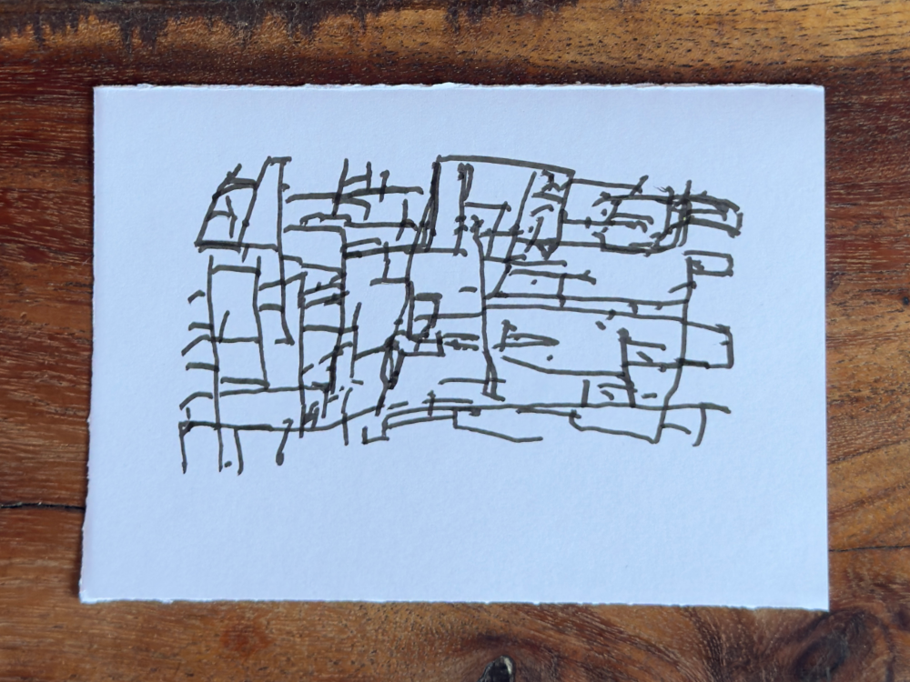 Line-us drawing on a card on a wooden table — a dense mesh of short, wobbly straight segments forming irregular cells. Reads as bark, masonry, dried mud, or stone wall depending on the eye.