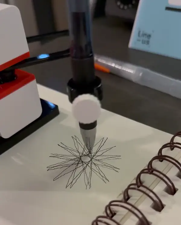 Line-us sped-up drawing a turtle-graphics star on a spiral notebook, wobble visible in every stroke